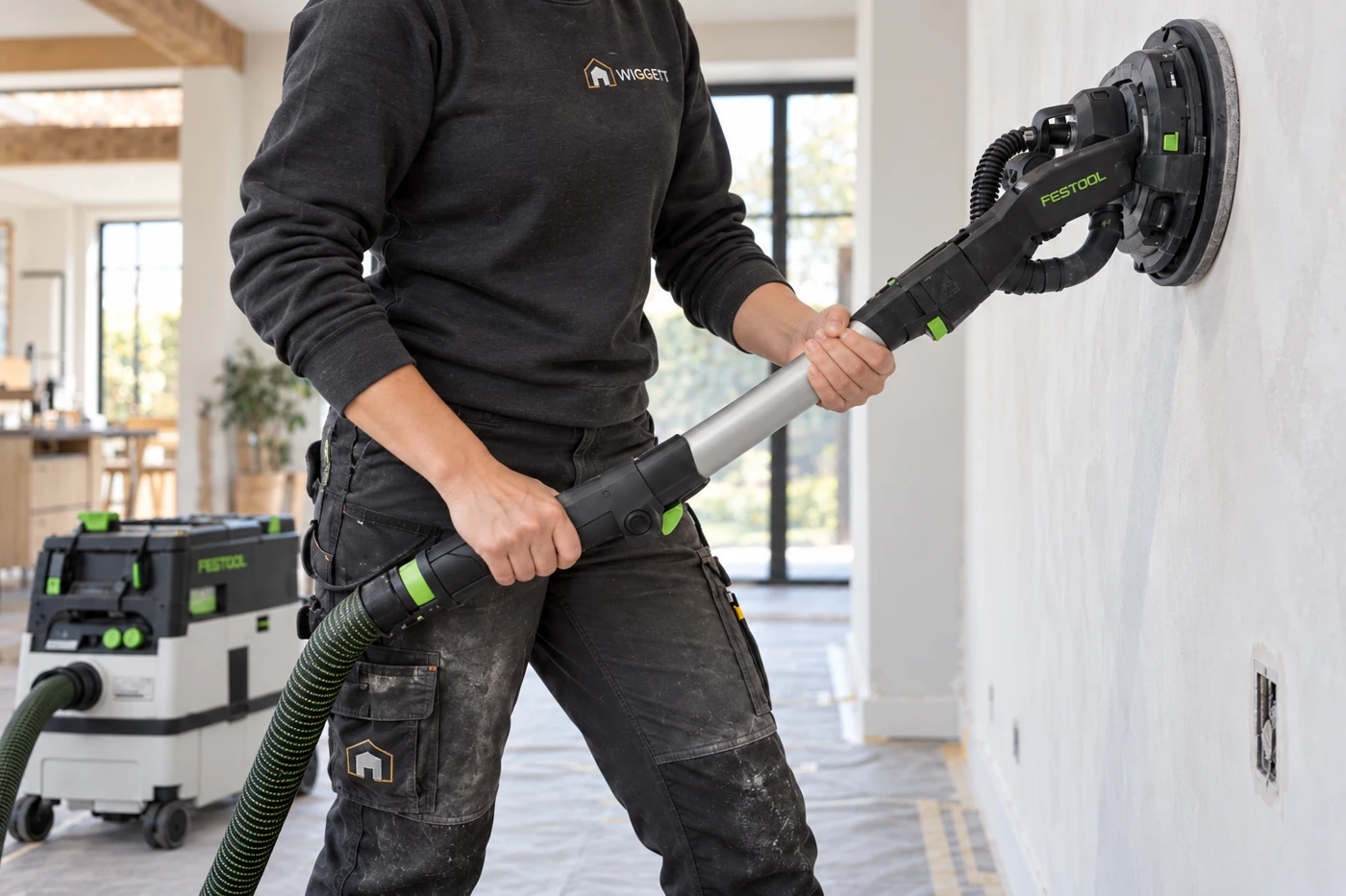 Vakman schuurt een wand met een Festool-wandschuurmachine en stofafzuiging
